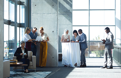 Front view of groups of diverse colleagues interacting with each other while other person are looking at mobile phone in modern office.