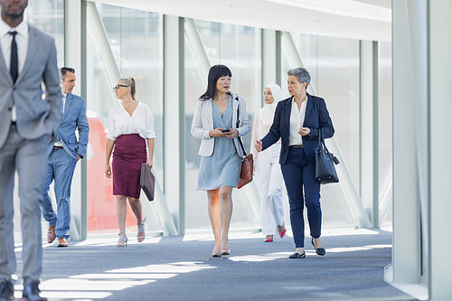 Front view of diverse businesswomen interacting with each other while walking in corridor in modern office