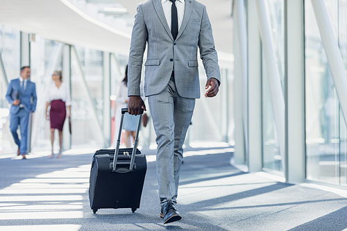 Low section of African american businessman walking in corridor with suitcase in modern office