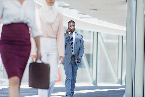 Front view of African american businessman walking in corridor while talking in mobile phone in modern office