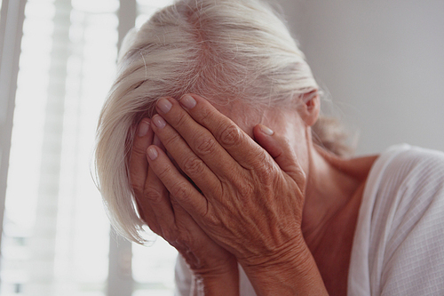 Side view of sad active senior Caucasian woman covering face with her hands at home