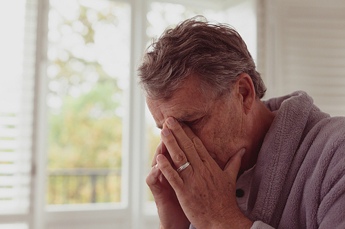 Front view of sad active senior Caucasian man with hands on face in a comfortable home