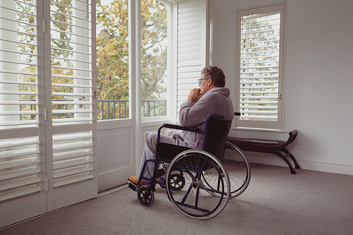 side view of thoughtful . active senior caucasian man looking through window on wheelchair in a comfortable home