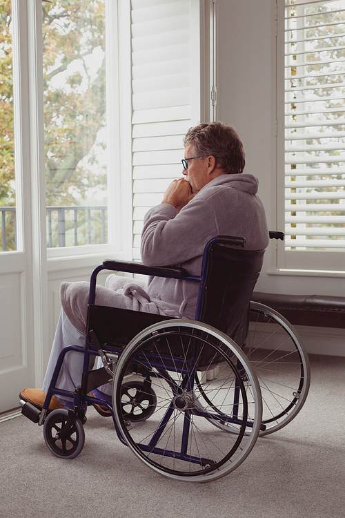 side view of thoughtful . active senior caucasian man looking through window on wheelchair in a comfortable home