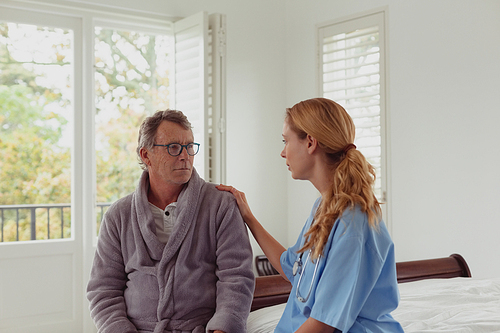 Front view of beautiful Caucasian female doctor consoling active senior man in a comfortable home
