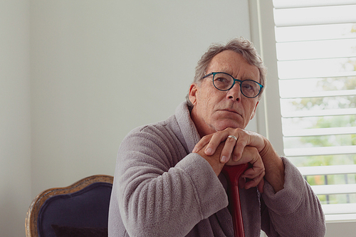 Front view of thoughtful active senior Caucasian man leaning on walking cane in a comfortable home