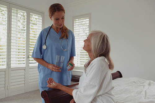 Mid section of Caucasian female doctor giving medicine to active senior woman in bedroom at home