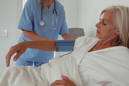 Front view of Caucasian female doctor checking blood pressure of active senior woman in bed in bedroom at home