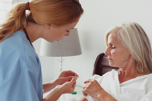 side view of caucasian female doctor talking to . active senior woman about her hearing aid on bed in bedroom at home