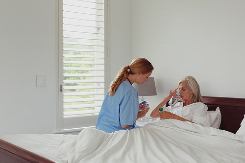 Side view of Caucasian female doctor giving medicine to active senior woman in bedroom at home