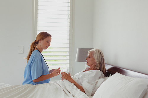 Side view of Caucasian female doctor giving medicine to active senior woman in bedroom at home