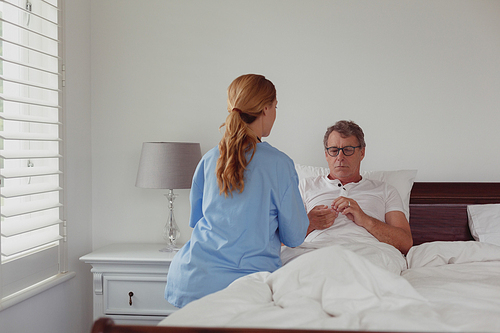 rear view of caucasian female doctor talking to . active senior man about his hearing aid in bed in bedroom at home