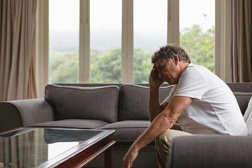 Side view of tensed active senior Caucasian man with hand on forehead sitting on sofa in a comfortable home