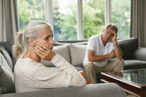 Side view of tensed active senior Caucasian woman with hand on face sitting on sofa in a comfortable home