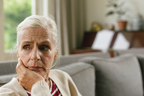 Front view of tensed active senior Caucasian woman with hand on face sitting on sofa in a comfortable home