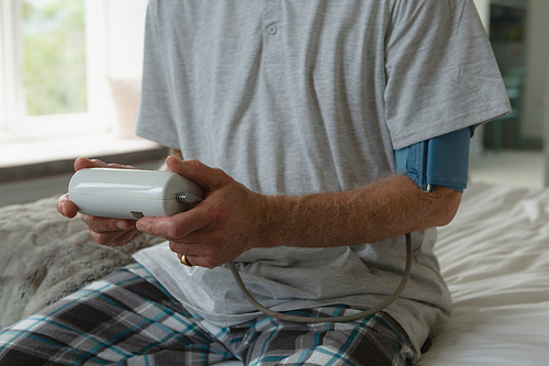 Mid section of active senior Caucasian man measuring blood pressure with sphygmomanometer in bedroom at home