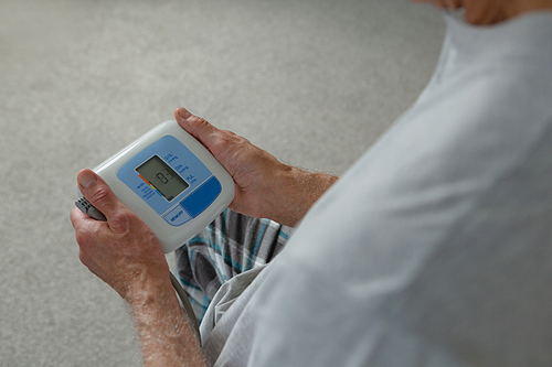 Mid section of active senior Caucasian man measuring blood pressure with sphygmomanometer in bedroom at home
