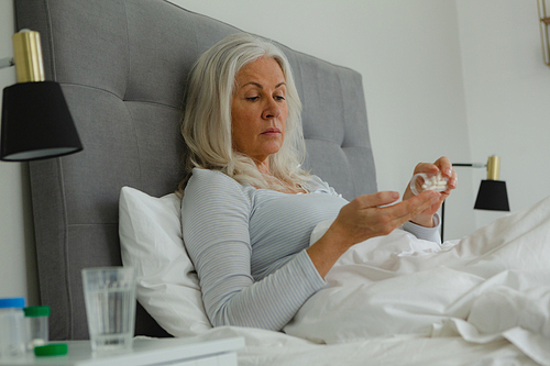 Side view of active senior Caucasian woman taking medicine in bedroom at home