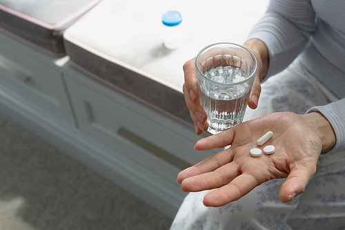 Mid section of active senior Caucasian woman taking medicine in bedroom at home