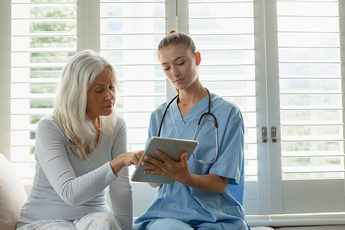 Front view of active senior Caucasian woman and female doctor using digital tablet on window seat at home