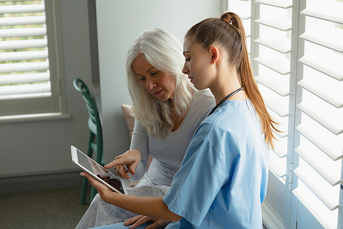 Side view of active senior Caucasian woman and female doctor using digital tablet on window seat at home