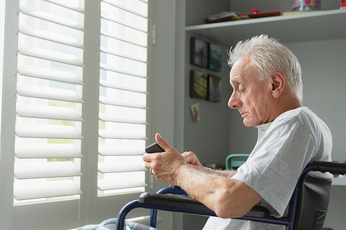 Side view of active senior Caucasian man in wheelchair using mobile phone at home