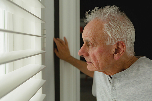 Side view of thoughtful active senior Caucasian man looking through window at home