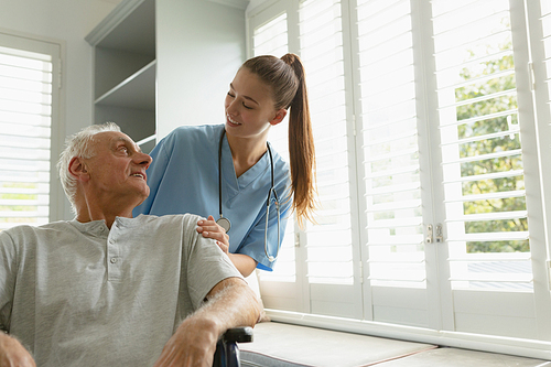 Front view of happy Caucasian female patient with active senior man in wheelchair at home