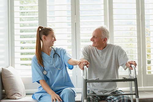 Front view of Caucasian female doctor consoling active senior man on window seat at home