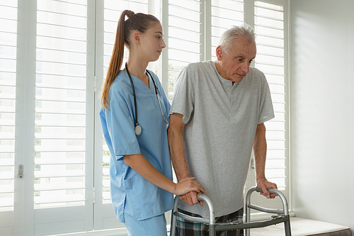 Side view of Caucasian female doctor helping active senior man to walk with walker at home