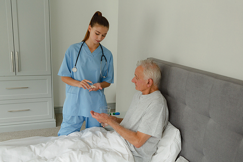 Side view of Caucasian female doctor giving medicine to active senior patient in bedroom at home