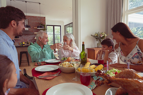 Front view of multi-generation Caucasian family toasting glasses of champagne on dining table at home