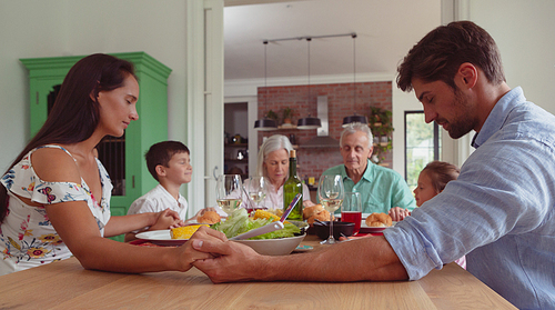 Front view of multi-generation Caucasian family praying before having food on dining table at home