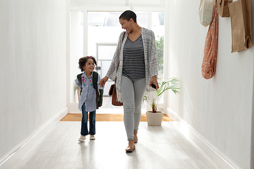 Front view of Happy African american girl with her mother walking together hand in hand near doorway at home