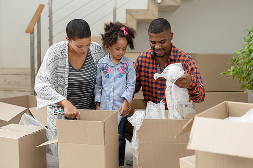 Front view of happy African american family unpacking cardboard boxes in living room at home