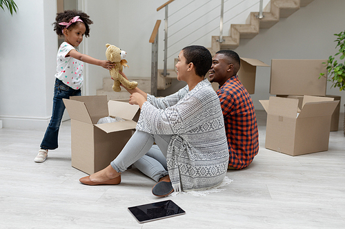 Side view of happy African american girl giving teddy bear to mother in living room at new home
