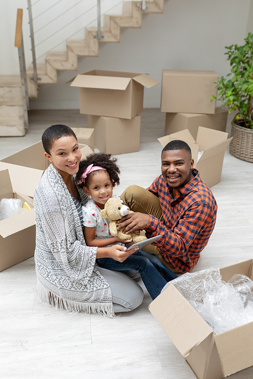 Front view of happy African american family using digital tablet while unpacking cardboard boxes in living room at home