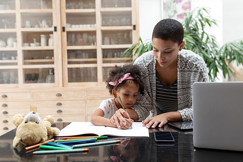 Front view of African american mother helping her daughter with her homework on a table at home