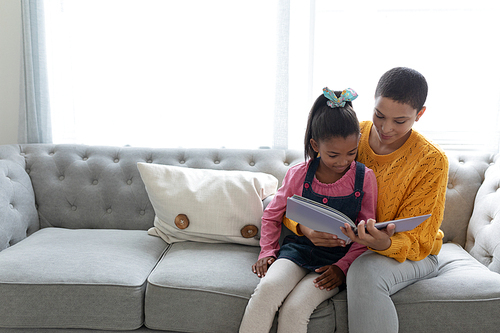 Front view of African american mother and daughter reading a story book on a sofa in living room at home