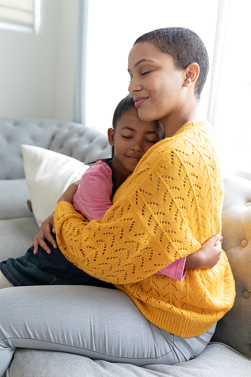 Side view of African american mother and daughter embracing each other on a sofa in living room at home