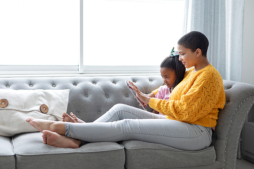Side view of African american mother and daughter using digital tablet in living room at home