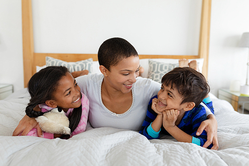 Front view of African american Mother and children relaxing together on bed in bedroom at home