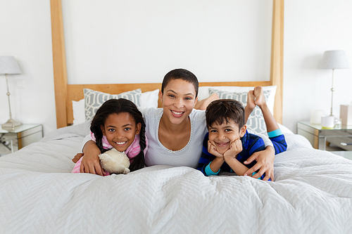 Portrait of African american mother and children relaxing together on bed in bedroom at home