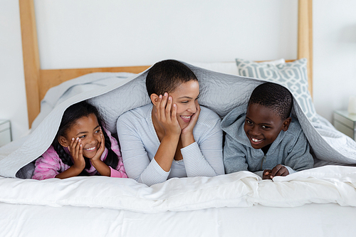 Front view of African american Mother and children relaxing under a blanket in bedroom at home