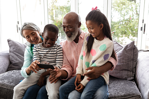 Front view of African american Multi-generation family looking at photos on mobile phone in living room at home