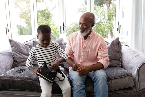 Front view of African american Grandfather and grandson sitting with virtual reality headset in living room at home