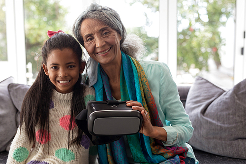 Front view of African american Grandmother and granddaughter sitting with virtual reality headset in living room at home