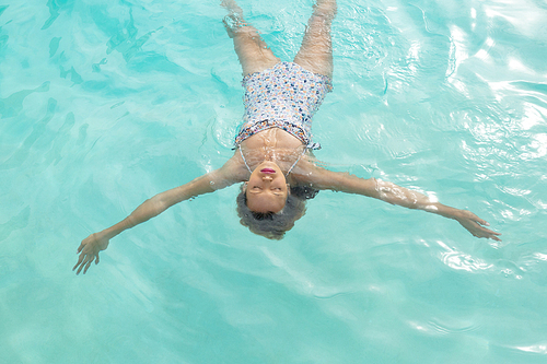 Overhead of Caucasian woman with eyes closed floating in swimming pool at the backyard of home. Summer fun at home by the swimming pool