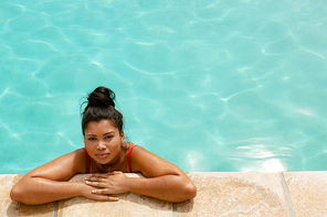 High angle portrait of  mixed-race woman standing at the edge of swimming pool in the backyard at home. Summer fun at home by the swimming pool
