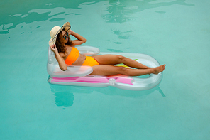 High angle view of mixed-race woman in bikini relaxing on a inflatable tube in swimming pool at the backyard of home. Summer fun at home by the swimming pool